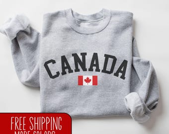 May include: Gray sweatshirt with the word "CANADA" in black block letters and a Canadian flag graphic.