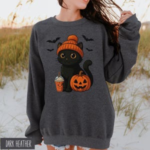 May include: Dark heather gray sweatshirt featuring a cartoon black cat wearing an orange beanie, with a pumpkin and a coffee drink. The design includes bats and is perfect for Halloween.