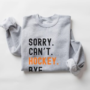 May include: Gray sweatshirt with the text "SORRY. CAN'T. HOCKEY." in black with the word "HOCKEY" in orange.
