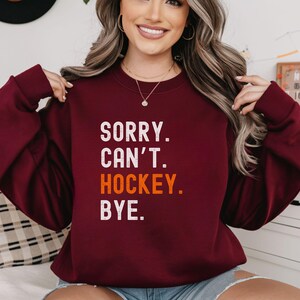 May include: A maroon sweatshirt with the text "SORRY. CAN'T. HOCKEY. BYE." in white with the word "HOCKEY" in orange.