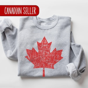 Peut inclure: Un sweat-shirt gris avec un motif de feuille d'érable canadienne rouge usé.