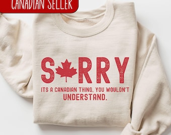 May include: A beige sweatshirt with a red graphic that says "SORRY" with a Canadian maple leaf in the "O". The text below the graphic says "ITS A CANADIAN THING, YOU WOULDN'T UNDERSTAND."