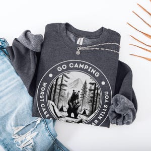 Puede incluir: Una sudadera gris oscura con un gr&aacute;fico blanco de un oso en un bosque con el texto "Go Camping Worst Case Scenario Bear Kills You".