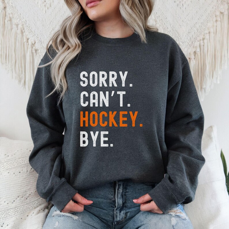 May include: A dark gray sweatshirt with the text "SORRY. CAN'T. HOCKEY. BYE." in white and orange lettering.