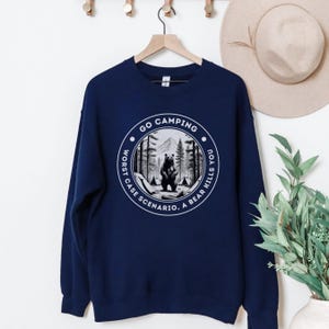 Puede incluir: Sudadera azul marino con un gr&aacute;fico blanco de un oso en un bosque con el texto "Go Camping. Worst Case Scenario. A Bear Kills You."