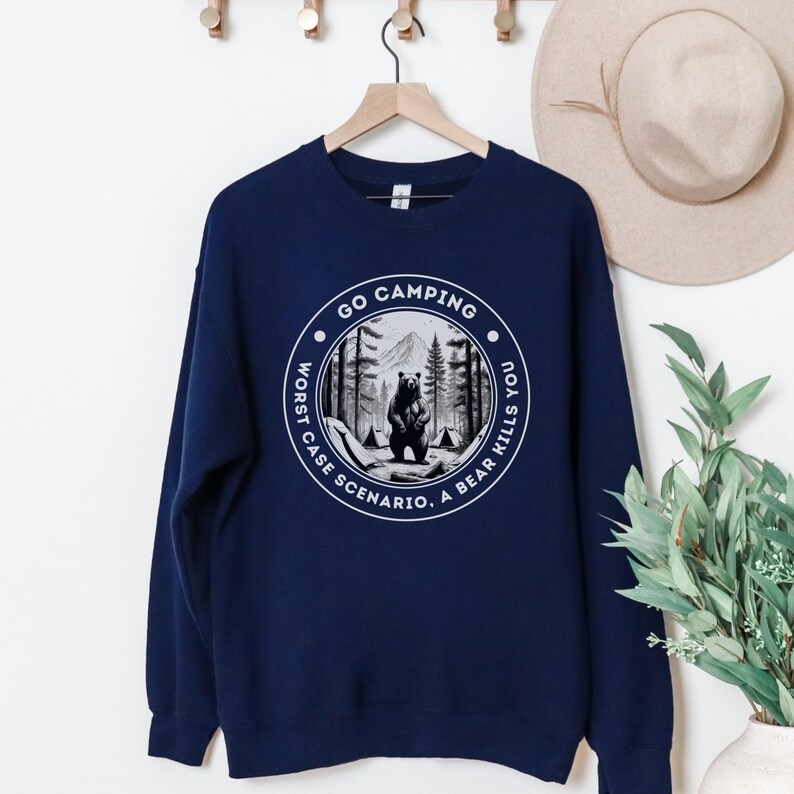 Puede incluir: Sudadera azul marino con un gr&aacute;fico blanco de un oso en un bosque con el texto "Go Camping. Worst Case Scenario. A Bear Kills You."