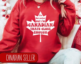 May include: Red sweatshirt with a white maple leaf design. The text on the sweatshirt reads "I'm not perfect but I'm Canadian that's close enough".