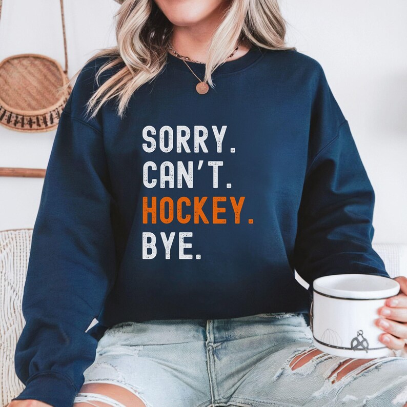 May include: A navy blue sweatshirt with the text "SORRY. CAN'T. HOCKEY. BYE." in white and orange lettering.