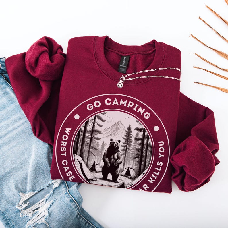 Puede incluir: Sudadera color burdeos con un gr&aacute;fico blanco de un oso en un bosque con el texto "Go Camping Worst Case Bear Kills You".