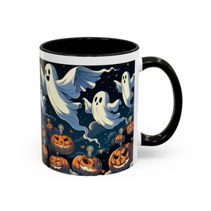 Puede incluir: Taza de cerámica blanca con interior y asa negros. La taza presenta un diseño temático de Halloween con fantasmas de dibujos animados, calabazas y un fondo de cielo nocturno azul oscuro. El diseño está impreso en el exterior de la taza.