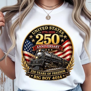 May include: A white t-shirt featuring a circular graphic with a black steam locomotive, the United States flag, and gold text reading United States 1776-2026 250th Anniversary, 250 Years of Freedom, and Big Boy 4014, framed by gold laurel leaves.
