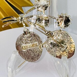 May include: A silver-toned metal brooch featuring a cluster of three circular elements attached to stems. The back of the brooch displays a textured finish with a horizontal pin mechanism and a clearly visible stamped hallmark on the left side.