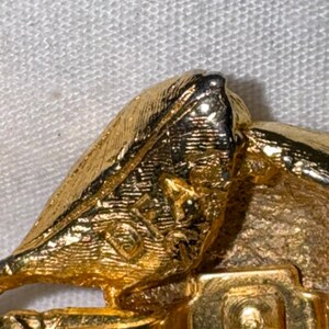 K&ouml;nnte beinhalten: Eine goldfarbene Metallbrosche mit strukturierter Oberfl&auml;che und einem sichtbaren Stempel mit der Aufschrift 'DORLAN' auf der R&uuml;ckseite, inklusive eines sicheren Nadelmechanismus an der Basis.