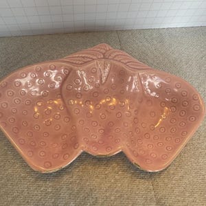 Könnte beinhalten: Eine rosa Keramik Schale in Form von drei Erdbeeren. Die Schale hat eine strukturierte Oberfläche mit kleinen Kreisen.