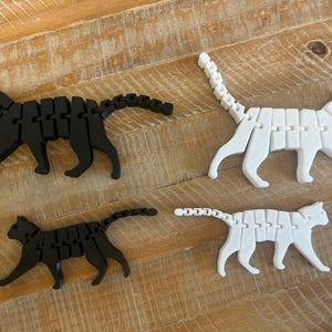 May include: Four articulated cat toys, two black and two white, made of plastic. The cats are posed in a walking position.