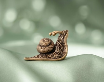 Könnte beinhalten: Eine kleine Schneckenfigur aus metallischem, bronzefarbenem Material mit einer strukturierten, noppigen Oberfläche am Körper und einem detaillierten, spiralförmigen Gehäuse. Die Schnecke ist im Seitenprofil mit zwei ausgestreckten Augenstielen zu sehen.