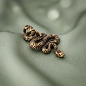 May include: A brass-toned metal pendant shaped like a coiled snake with a textured, scale-like surface. The snake's body curves into a loop at the top, which is topped with a small, detailed skull design that serves as the bail for the pendant.