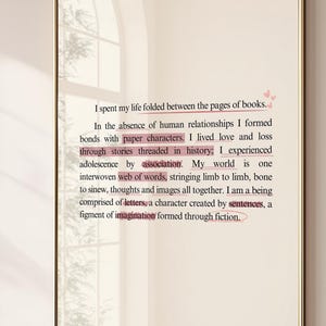 May include: A rectangular mirror with a gold frame displays text from a book. The text is in black, with some words highlighted in pink. The mirror is hanging on a light pink wall.