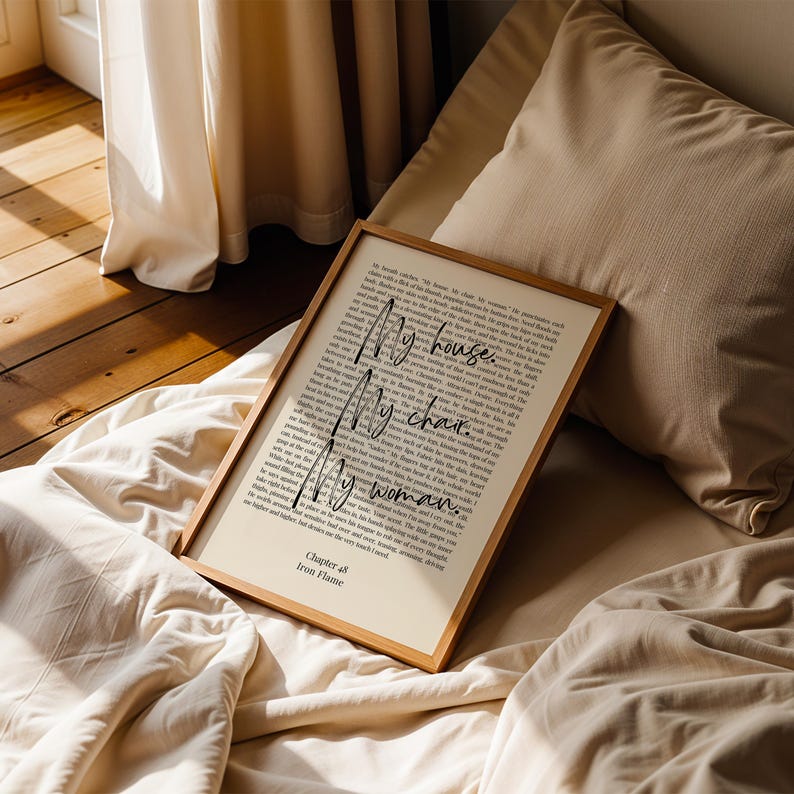 Puede incluir: Una impresi&oacute;n enmarcada con las palabras "My house. My chair. My woman." en una fuente manuscrita. La impresi&oacute;n est&aacute; en un marco de madera clara y descansa sobre una cama con ropa de cama beige. El texto "Chapter 48 Iron Flame" est&aacute; en la parte inferior.
