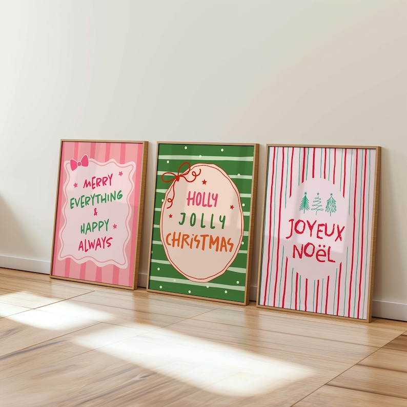 May include: Three framed Christmas art prints. The prints feature festive text in pink, green, and red, with phrases like "Merry Everything & Happy Always," "Holly Jolly Christmas," and "Joyeux No&euml;l." The frames are a natural wood color.