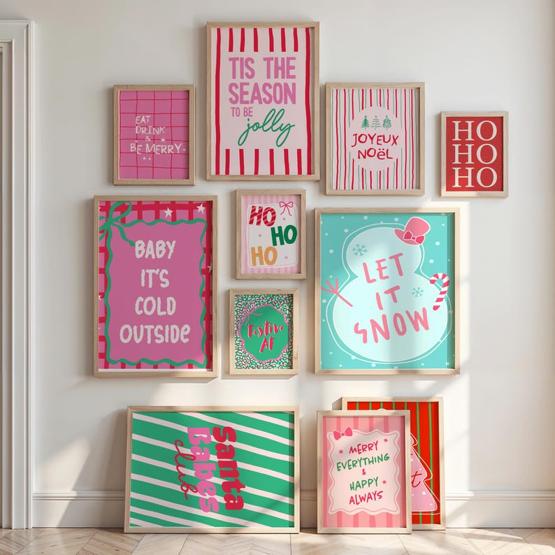 May include: A collection of framed Christmas-themed art prints. The prints feature festive phrases like "Let it Snow," "Baby It's Cold Outside," and "Tis the Season to be Jolly." The color palette includes pink, red, green, and blue, with wooden frames.
