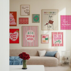 May include: A collection of framed Christmas-themed art pieces displayed on a wall above a beige sofa. The art features festive phrases like "Peace Love Joy", "Joyuex Noel", and "Tis the Season to be Jolly". The room is decorated in a modern style.