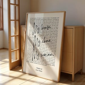 Puede incluir: Una impresi&oacute;n enmarcada con el texto manuscrito "My house. My chair. My woman." y texto del cap&iacute;tulo 48 de "Iron Flame". El marco es de color marr&oacute;n claro. La impresi&oacute;n se muestra en interiores.