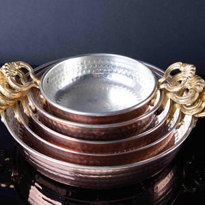 May include: Set of four copper bowls with a hammered finish and gold-tone handles. The bowls are nested inside each other.