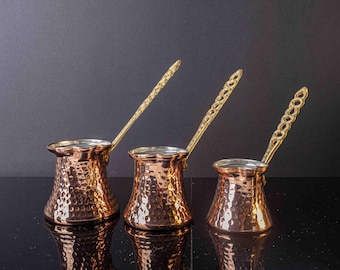 May include: Three copper coffee pots with gold handles. The pots are of different sizes and have a hammered texture.