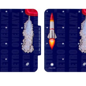 May include: Two blue and red game overlays for the ColecoVision video game console. The overlays feature a rocket ship with a red nose and white body, and a trail of smoke behind it. The text "RETRO OVERLAYZ" is printed on the overlays.