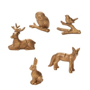 May include: A collection of gold-colored animal figurines, including a deer, owl, bird, fox, and rabbit. The deer is lying down, the owl is perched on a branch, and the bird is on a branch. The fox and rabbit are standing.