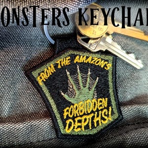 May include: A black and green keychain with a monster hand and the text "From the Amazon's Forbidden Depths!"