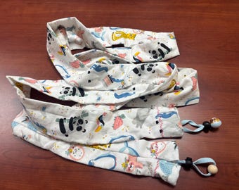 May include: White fabric headbands with a colorful animal print featuring pandas, toucans, and elephants. Each headband has a light blue drawstring with a wooden bead and a black bead.