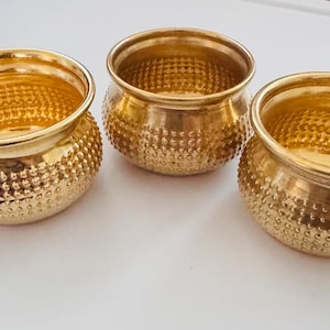 May include: Three small, round, gold-coloured metal bowls with a polished finish. Each bowl features a wide, smooth rim and a textured exterior surface covered in a repeating pattern of small, raised dots that extend from the base to the rim.