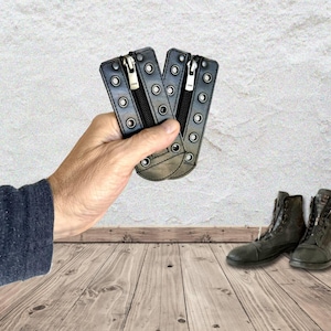 May include: Two black leather boot lace-up zipper inserts featuring silver-toned metal eyelets and a central black zipper closure with a YKK pull tab. These rectangular accessories are designed to be attached to the front of lace-up boots.