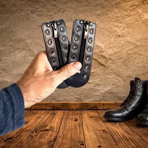 May include: Two black leather boot lace-in zipper inserts featuring silver-toned metal eyelets along the edges and a central vertical zipper closure. These rectangular attachments are designed to be laced into the front of boots.
