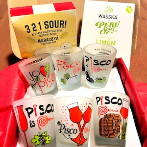 Puede incluir: Un juego de regalo con vasos de chupito esmerilados con "Pisco es Perú" y otros diseños, junto con cajas de mezclas "321 Sour!" y "Wasska Perú Sour". Los vasos de chupito tienen varias ilustraciones y texto.