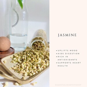 May include: A glass jar filled with dried jasmine flowers, spilling out onto a gold tray. The text "JASMINE" is written in black on a white background, with a list of benefits: "UPLIFTS MOOD", "AIDS DIGESTION", "RICH IN ANTIOXIDANTS", "SUPPORTS HEART HEALTH".