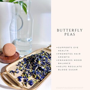 May include: Dried butterfly pea flowers on a gold tray. The flowers are blue and purple and have a green stem. The text on the image reads "Butterfly Peas" and lists the health benefits of the flowers, including supporting eye health, promoting hair growth, enhancing mood balance, and helping regulate blood sugar.