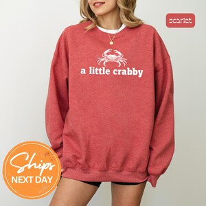 A woman wearing a red sweatshirt with the text "a little crabby" printed on it.
