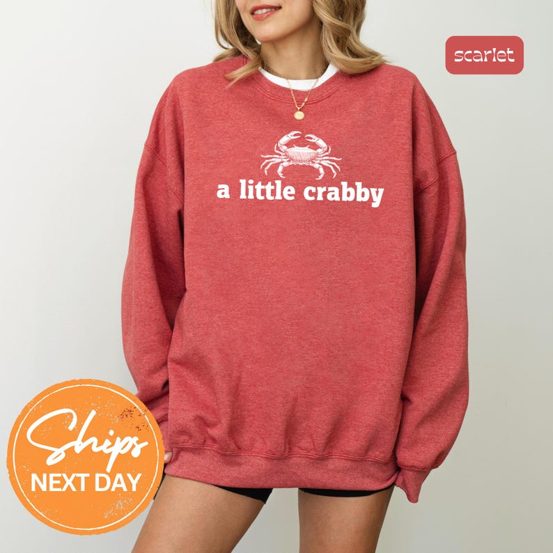A woman wearing a red sweatshirt with the text "a little crabby" printed on it.
