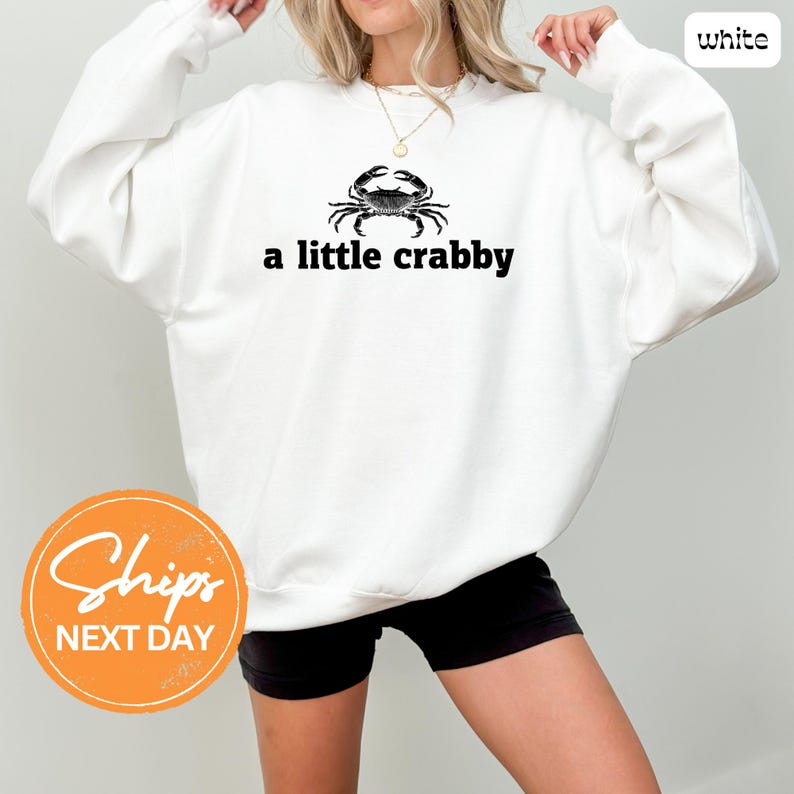 A woman wearing a white sweatshirt with a black crab design and the text "a little crabby" printed on it.