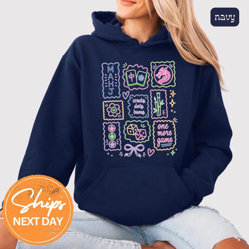 May include: A navy blue hooded sweatshirt featuring a colorful neon-style graphic print on the front. The design includes Mahjong tiles, a dragon, bamboo, dice, and text that reads MAHJ, cracks dots bams, and one more game in various colors.