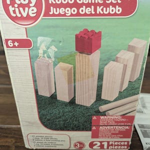 May include: A Playtive Kubb Game Set box featuring a graphic of light-colored wooden blocks and a red king piece on a green field. The packaging includes the text Playtive, Kubb Game Set, 6+, 21 Pieces, and safety warnings in English and Spanish.
