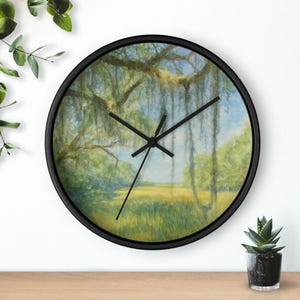 Puede incluir: Un reloj de pared redondo con marco negro. La esfera del reloj presenta una pintura de acuarela de un paisaje con árboles, hierba y cielo azul. Las manecillas del reloj son negras.