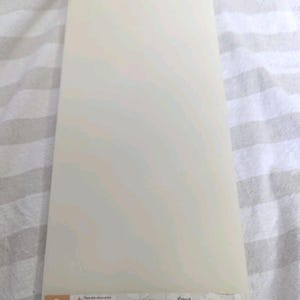 May include: A rectangular off-white Cricut Cuttlebug A Plate spacer with a smooth surface. The bottom edge features a label with the letter A, instructions in multiple languages, and the text Cricut cuttlebug A Plate - Spacer printed in black.