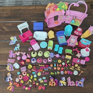 May include: A collection of plastic toy playsets, miniature furniture, and small pony figurines. The set includes a pink house structure, various chairs, beds, tables, and numerous tiny accessories like hangers, food items, and small decorative pieces.
