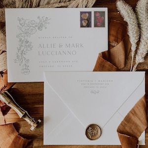 May include: Two white wedding invitation envelopes with floral designs and stamps, one sealed with a gold wax seal. The envelopes are on a wooden tray with fabric and dried flowers. The text on the envelope reads "Allie & Mark Lucciano".