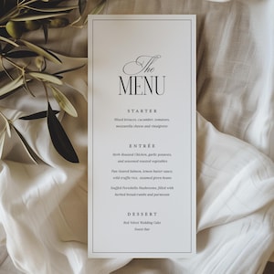 May include: A rectangular menu card with the word "The MENU" in elegant script at the top. The menu lists a starter, entree, and dessert. The card is white with a black border and text, set against a soft, neutral background.