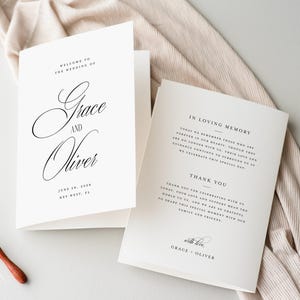 May include: Wedding stationery set. A folded invitation card with the names "Grace and Oliver" in script, and a second card with text. Gold wax seals and a wax melting spoon with a wooden handle are also present.